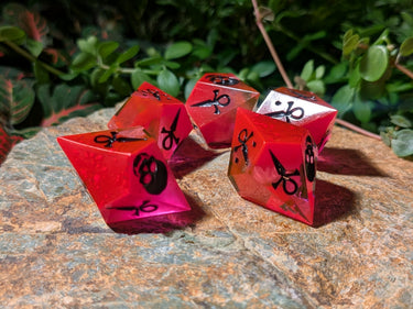 Red and clear dice with black symbols on a stone surface with greenery in the background
